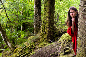 Conteuse cachée derrière un arbre, au milieu d'une forêt, faisant le signe du silence