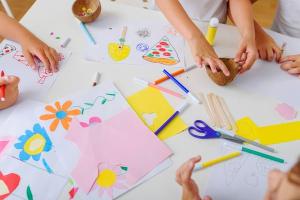 Photo d'une table recouverte de dessins, feutres et ciseaux avec des mains en train de bricoler